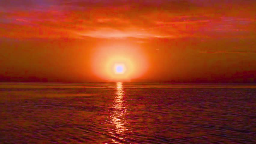 Vibrant orange sunset over calm sea, sun reflection shimmering, dramatic sky, atmospheric view.