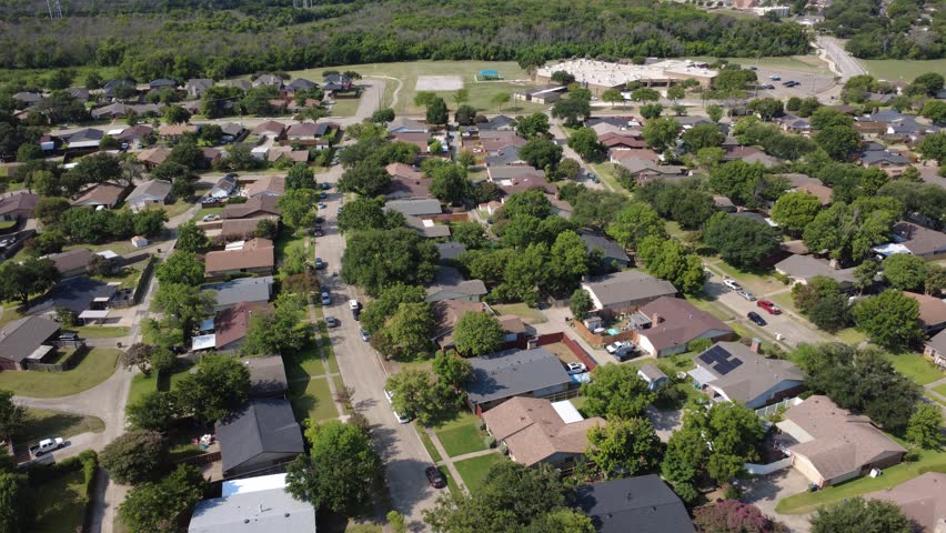 Shady avenues in Lyons Crest Estates within Dallas Fort Worth suburbs curve past neat lawns, leading toward public middle school grounds. Service trucks personal vehicles park along Garland, TX. USA