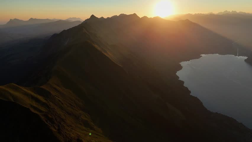 Drone view of warm sunrise illuminating the Augstmatthorn mountain ridge above Lake Brienz in the Swiss Alps.