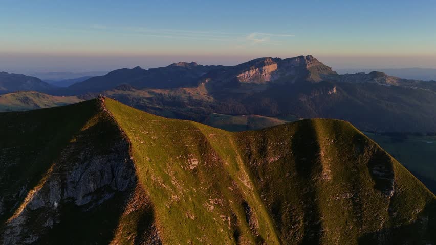 Drone view of golden morning light illuminating the rugged grassy ridge of Augstmatthorn in the Swiss Alps.