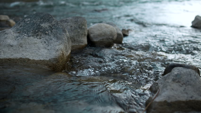 Crystal clear freshwater stream flowing among stones and rocks in a mountain landscape, capturing natural beauty, clean spring water, and refreshing outdoor scenery.