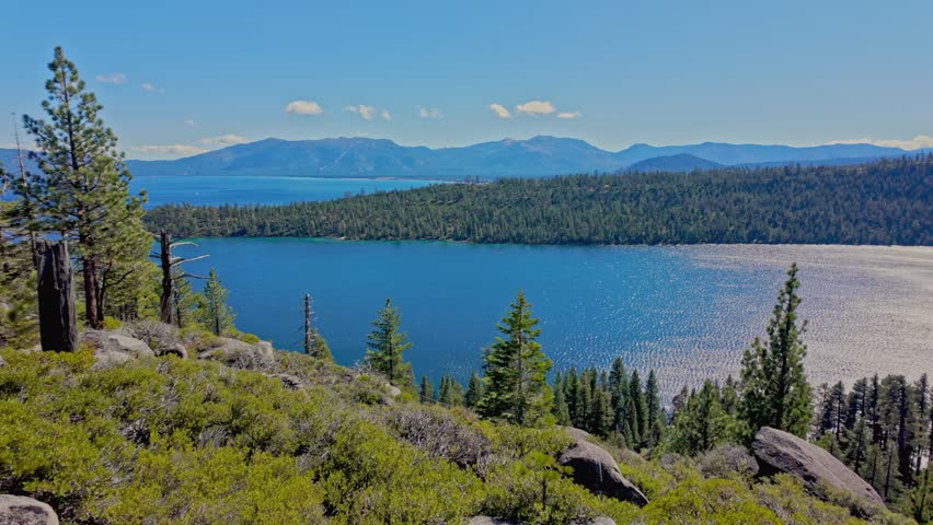 Panoramic view of Lake Tahoe with deep blue water, pine forest and Sierra Nevada mountains. Sunlight reflects on the lake surface, creating a peaceful and scenic natural landscape in California