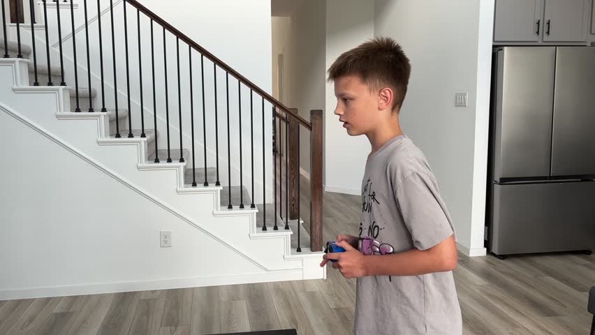 A boy actively jumping and moving while intensely engaged in a video game, operating a blue controller in a modern home.
4K horizontal video.