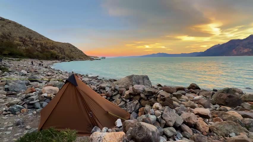 Beautiful evening landscape shot of a solo backcountry tent set up on a rocky glacial lake shore during sunset in Argentine Patagonia.