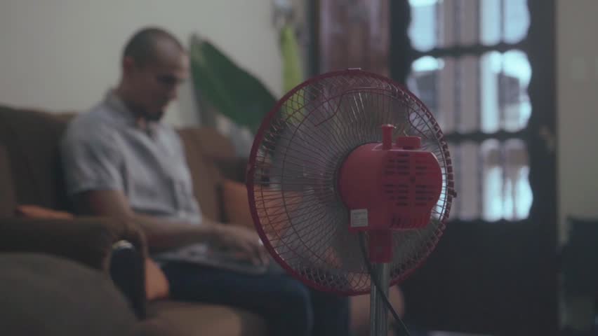 Electric floor fan cooling the air with a person working on a laptop in the background