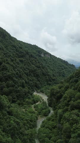Vertical aerial drone footage of a rocky forested mountain above the Abasha River, with the Kaghu Waterfall flowing into the river below in the Egrisi Range, Georgia.