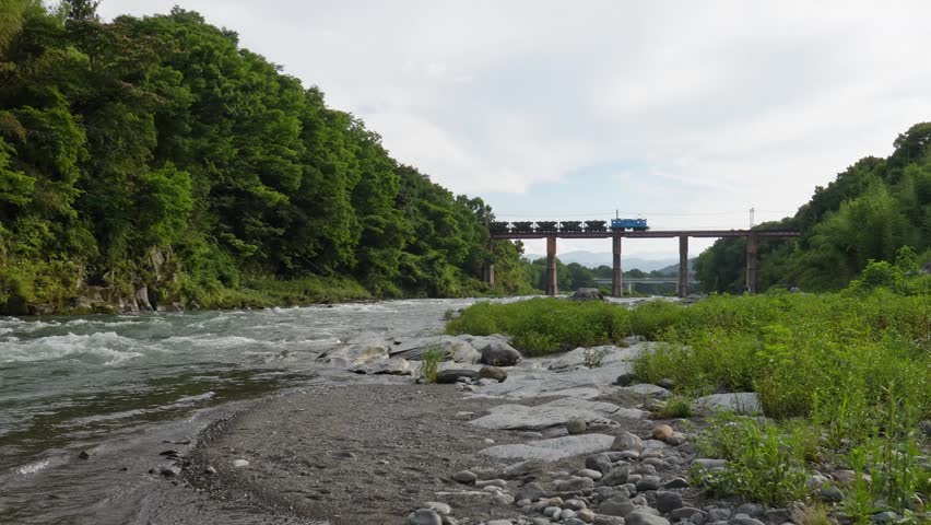 A Chichibu Railway freight train crossing the Arakawa Bridge in Nagatoro, set against the backdrop of the clear river.