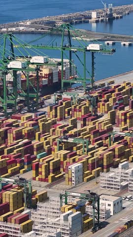 A container terminal with numerous shipping containers stacked and ready for transport. Cranes move cargo at the facility located near the water.