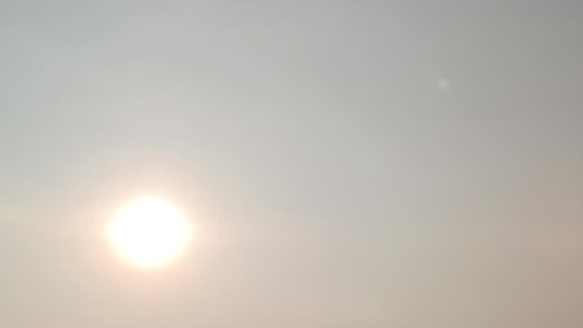 Silhouette of a bird flying past a bright sun in a hazy sky.