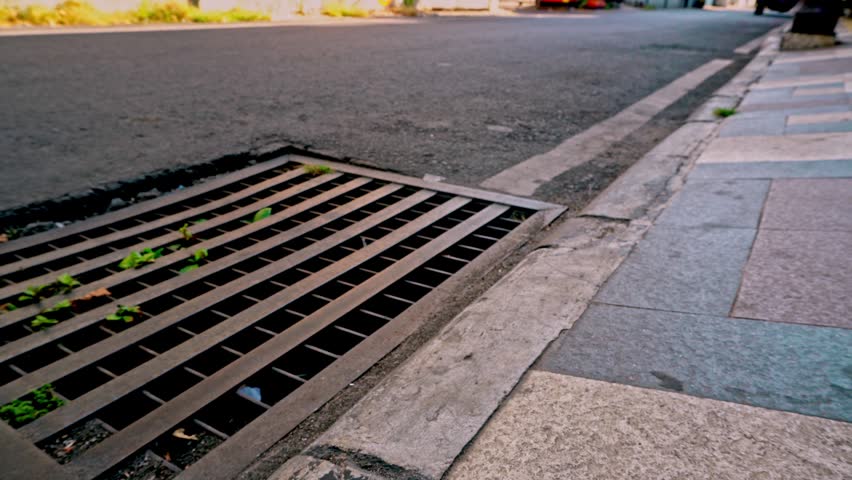 Smooth sliding camera movement to the left capturing a metal drainage grate on a city street in the historic old town district of Gresik, Indonesia.