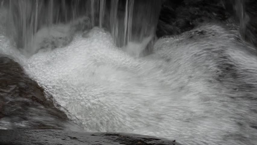 Close Up of Powerful Rushing Water in a Natural Waterfall with White Foam and Bubbles Splashing Down