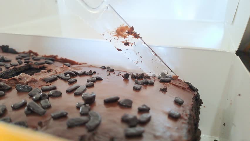 Close up hand cutting chocolate brownie with frosting and sprinkles in box. Fudgy dessert, chocolate cake, sweet treat, bakery, indulgence, food.