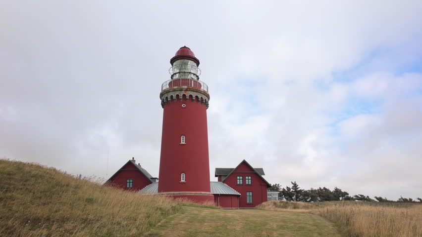 The iconic red lighthouse Bovbjerg Fyr with attached houses on grassy coastal dunes under a cloudy sky