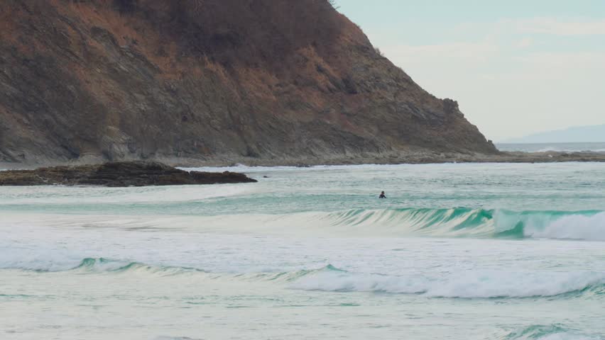 Gentle turquoise waves roll onto the secluded beach of Playa Barrigona beneath rugged tropical cliffs on Costa Rica