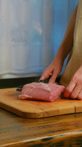 Close-up view of cutting pork fillet into chops on wooden cutting board in the kitchen