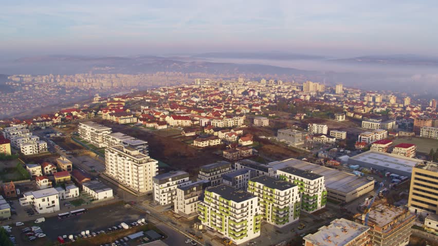 Aerial drone view of Cluj-Napoca, Romania at sunrise, showing modern apartment buildings, houses, and distant fog