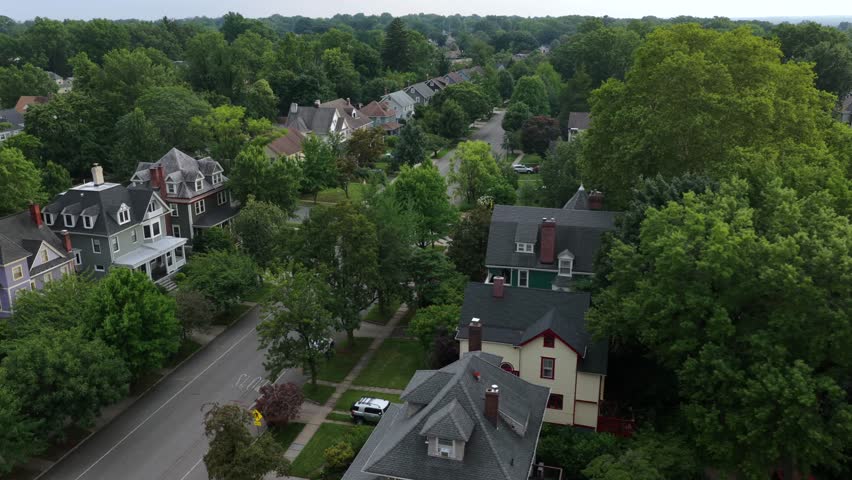 Victorian style houses with turrets line tree shaded street near Seton Hall in South Orange, New Jersey, dense green canopy covers quiet residential neighborhood streets. Aerial drone flyover shot