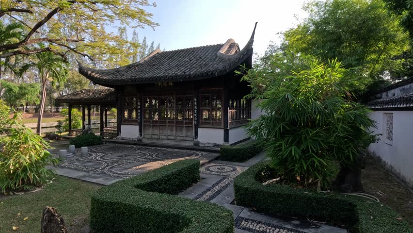 Wide shot of a traditional Japanese-style pavilion with black tiled roof and decorative stone mosaic floor in a Bangkok city park on a bright sunny day.