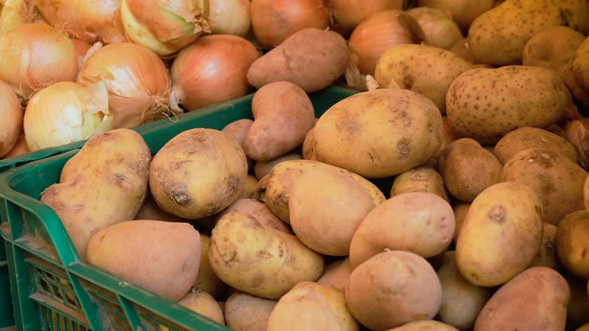 Rustic potatoes and onions in green crates at open air market stall. Unwashed root vegetables ready for sale. Farm produce, grocery shopping and local agriculture concept