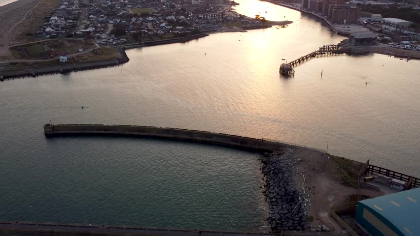 Drone shot rising up to reveal a river going through a coastal town with the sun setting over the town