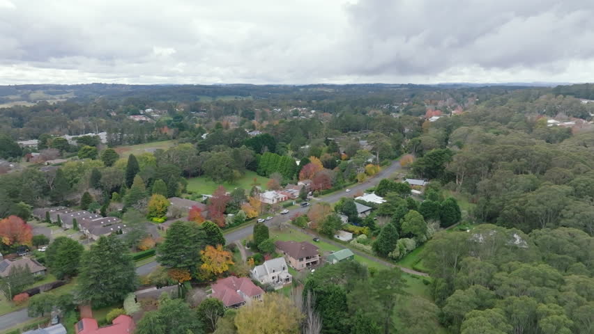 Drone aerial flying above tree-lined residential streets and homes in Bundanoon surrounded by native bushland in the Southern Highlands, New South Wales, Australia.