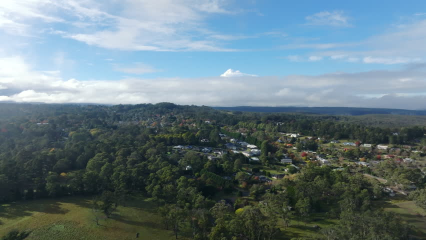 Wide drone aerial revealing Bundanoon nestled among rolling bushland and forests beneath expansive clouds in the Southern Highlands, New South Wales, Australia.