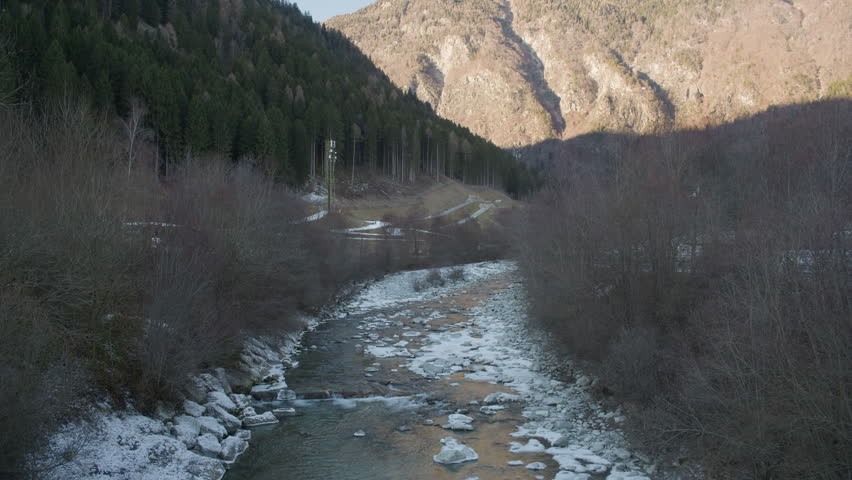 Mountain river stream forest landscape, tripod shot. High angle overview of fast alpine water creek flowing through green trees with big summits.