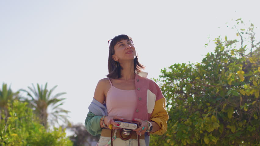 The girl with a camera in her hands takes a picture. A stylish girl walks through the city and shoots on the camera. She travels and creates content. The film of the camera. 