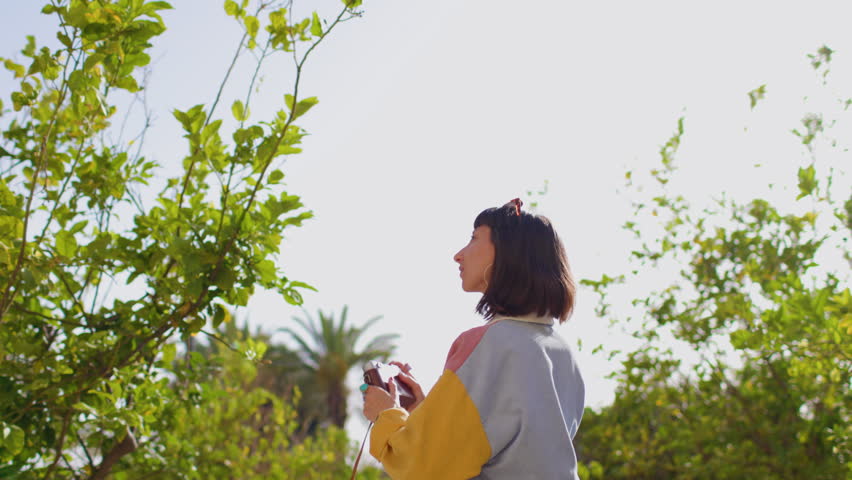 The girl with a camera in her hands takes a picture. A stylish girl walks through the city and shoots on the camera. She travels and creates content. The film of the camera. 