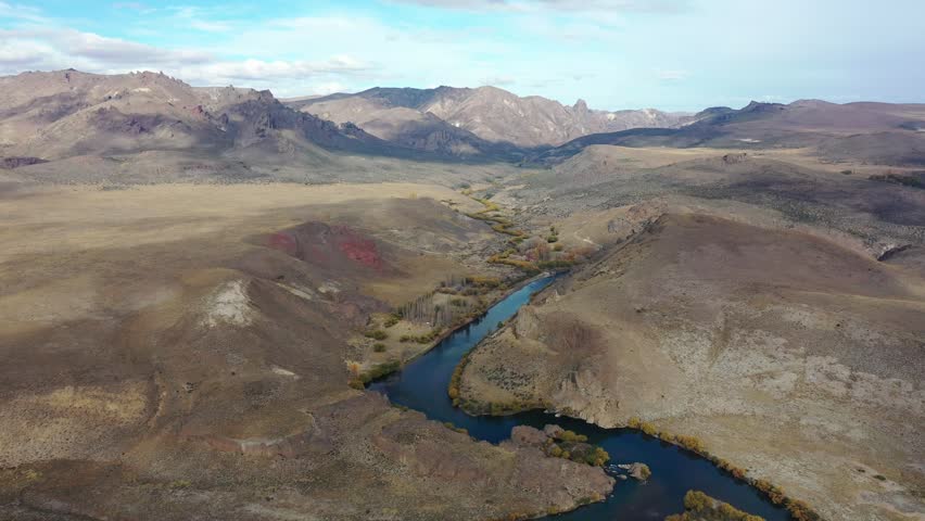 Aerial view of winding river running through desert mountain landscape, scenic nature scenery with rocky hills, wide angle landscape cinematography, outdoors exploration footage.
