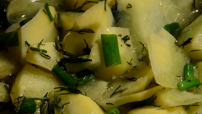 Sliced potato with dill is being prepared in a frying pan close-up