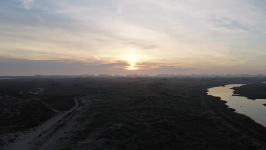 Drone ascends above the tidal wetlands of Terschelling, Friesland, Netherlands, revealing winding tidal channels, salt marshes, coastal grasslands and a glowing sunrise over the Wadden Sea.