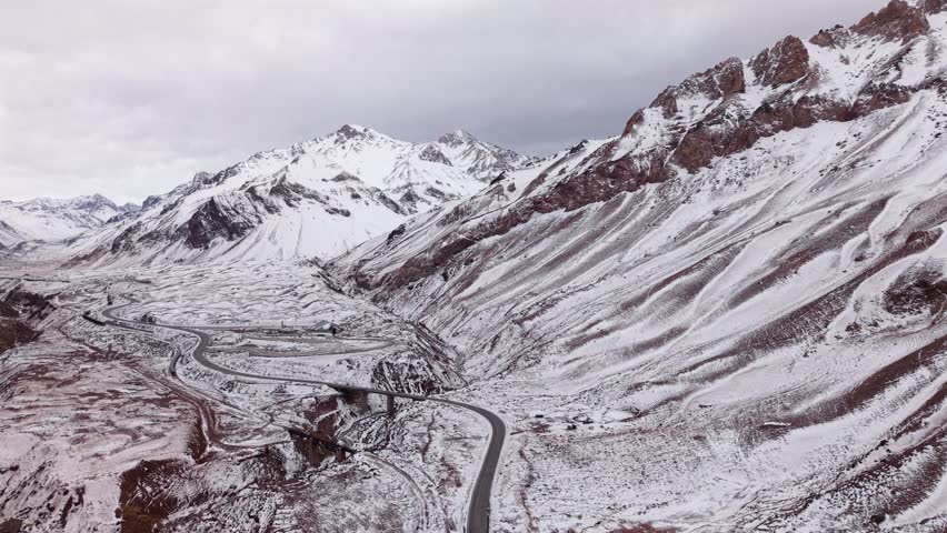 Breathtaking aerial footage of Route 7 winding through snow-dusted Andes near Puente del Inca, Mendoza, Argentina. Dramatic mountain terrain, crisp winter scenery.