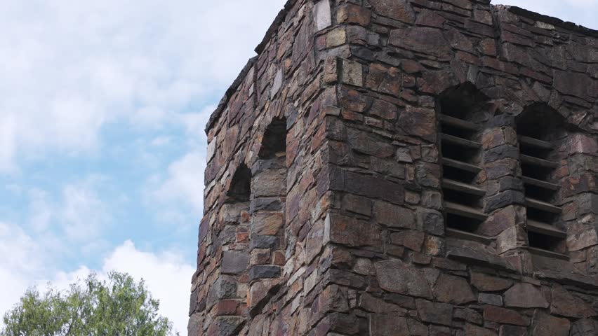 Camera slowly tilting down a historic stone church belfry against a cloudy sky