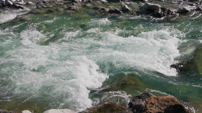 Mountain river blue water stream, gimbal stabilizer shot. Close up tracking view of crystal clear alpine creek rushing rapidly over white stones and rocks.