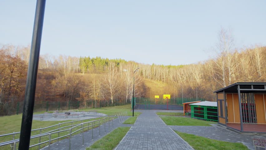 Paved stone walkway curves towards outdoor basketball court. Recreational park area features clean pathways and cozy wooden gazebos