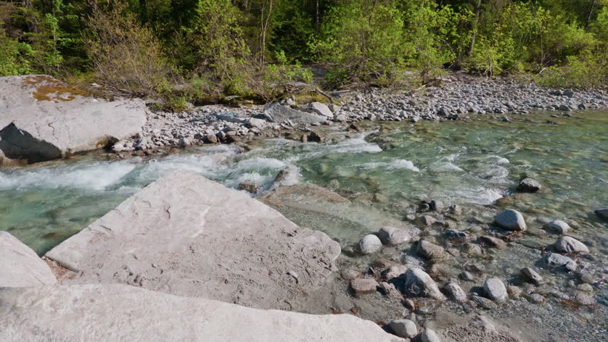 River forest white stones water, gimbal stabilizer shot. Moving sideways from left to right tracking clean stream flowing opposite way over wild rocks.
