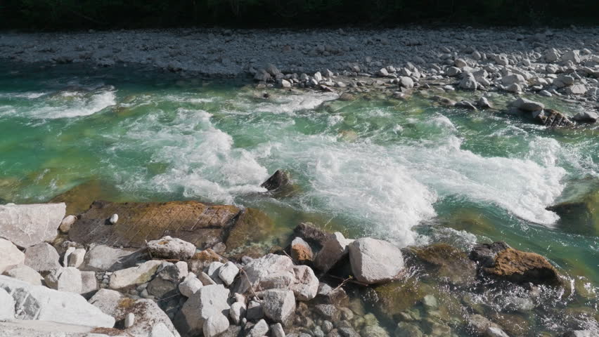 Mountain river blue water rocks, gimbal stabilizer shot. Moving sideways from left to right tracking powerful crystal stream rushing over white wild stones.