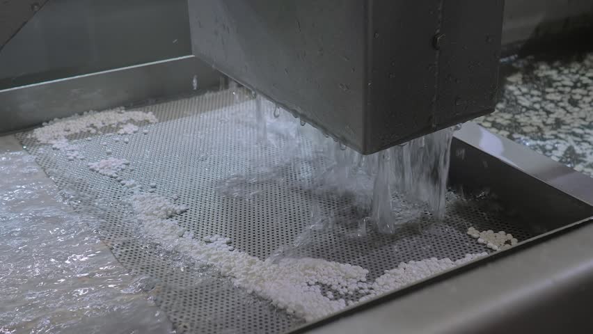 Close up: fast water flow with recycled plastic granules, pellets for filtration, separation the plastic material - plastic pelletizer recycling machine. Reuse, waste reduction and sustainable concept