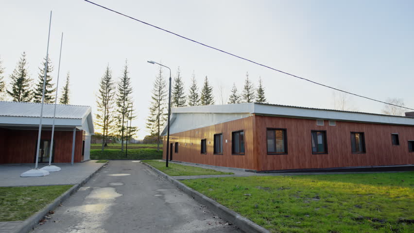 Residential pavilion with wooden siding stands along paved asphalt driveway. Pine trees line up behind country resort building in autumn