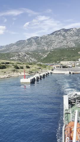 Ferry boat departing from Stinica port in Croatia and heading toward the island of Rab, with the dramatic mountain landscape of Northern Velebit visible in the background. Scenic Adriatic Sea crossing and transportation between the Croatian mainland and island of Rab.