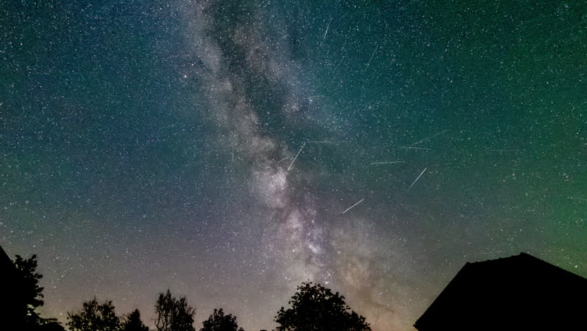 A stunning nighttime time lapse with a slow camera zoom in showing the Milky Way galaxy moving across the starry sky above a peaceful river surrounded by silhouettes of trees.
