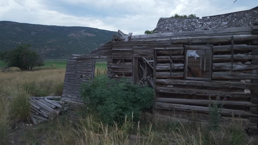 An old, dilapidated wooden house surrounded by overgrown grass and trees in Woodland, Utah.