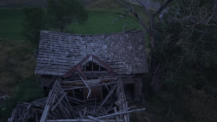 An aerial view of an old, dilapidated house surrounded by woodland in Utah during low light conditions.
