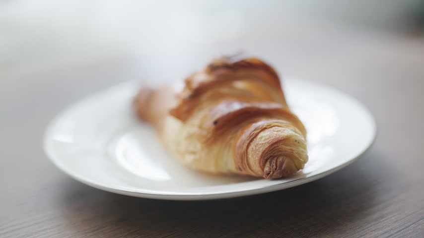 French croissant filled with rich, melt-in-your-mouth chocolate cream. Soft studio lighting highlights the delicate flaky pastry layers, crisp buttery crust, glossy dark chocolate filling oozing from the center, and a subtle dusting of cocoa powder. Ideal for bakery packaging