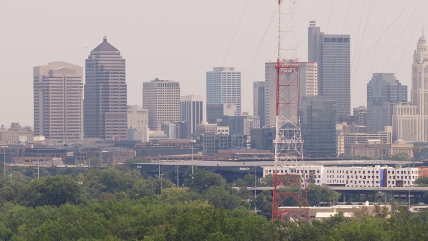 Moving shot and aerial view of Downtown Columbus Ohio with Scioto river, railroad tracks, large office buildings, interstate 670 i670 highway, and lush green trees on summer day from long lens drone
