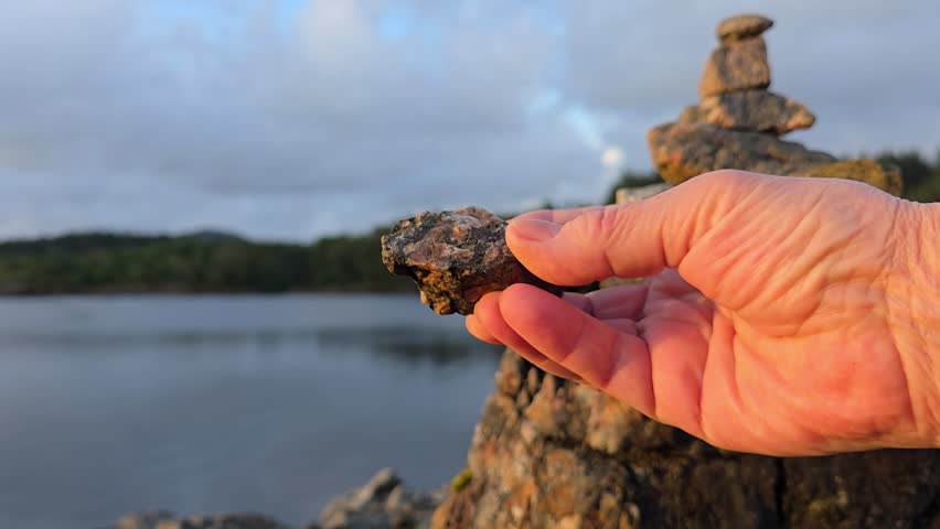 A hand   examines small stones for balancing rocks at sunset. Norway, Toska. August