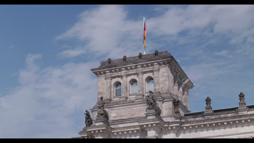 Close-up view of the historic Reichstag building with the German flag waving against a blue cloudy sky in Berlin, Germany.