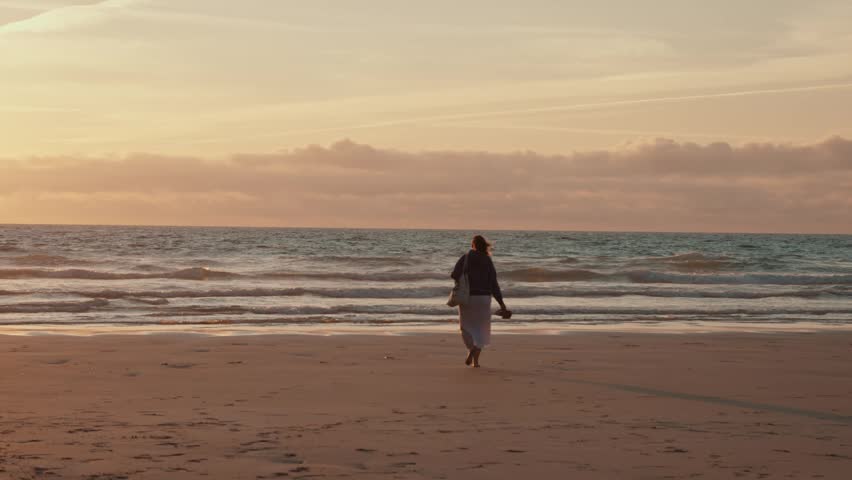Woman walking on a beach at sunset