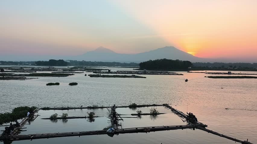 Beautiful morning sunrise at a tropical lake with mountain background and small silhouettes of fishing boats. 